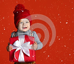 Portrait of a little boy in a red hat with a pompon. holding a large gift box with a white bow.