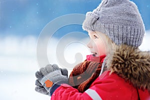 Portrait of little boy in red winter clothes having fun with snow