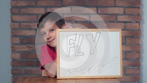 Child sitting at the desk holding flipchart with lettering fly o