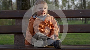 Portrait of little boy sitting on bench in park. Cute kid spending time outside.