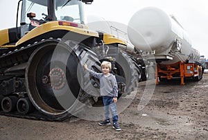 portrait of a little boy standing near the huge caterpillar wheels of a bulldozer