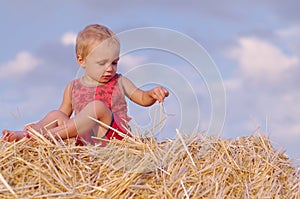 Portrait of little boy in a summer hat sitting on a haystack in a field of wheat