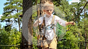 Portrait of little boy walking over rope strung between trees in scout camp. Active childhood, healthy lifestyle, kids playing