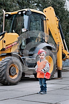 Portrait of little builder in hardhats working outdoors near Tractor excavator.