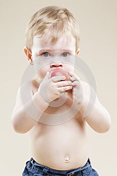 Portrait of Little Caucasian Child With Red Apple Fruit in Hands While Eating And Posing Against Beige Background