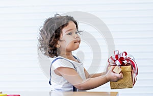 Portrait little caucasian curly hair girl wearing casual clothes, holding gift or present box with surprising face, while
