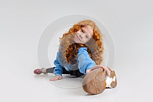 Portrait of little Caucasian cute girl sitting on a twine and posing isolated over gray studio background.