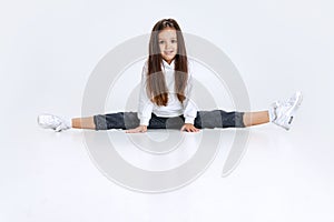 Portrait of little Caucasian cute girl wearing hoodie with jeans sitting on a twine and having fun isolated over white