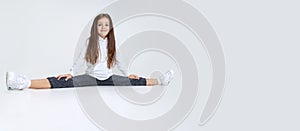 Portrait of little Caucasian cute girl wearing hoodie with jeans sitting on a twine and having fun  over white