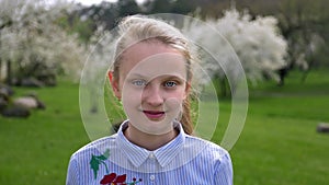 Portrait little Caucasian girl with blue eyes in beautiful shirt standing in the Park in springtime