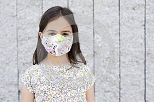 Portrait of little caucasian girl with face protection mask. She is standing next to a stone wall