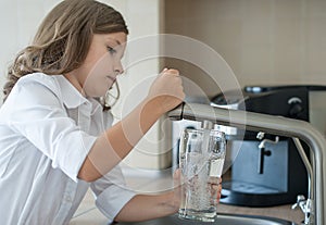 Portrait of a little caucasian girl gaining a glass of tap clean water. Kitchen faucet. Cute curly kid pouring fresh water