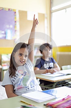 Portrait of little caucasian girl with raised hand in class. Primary education