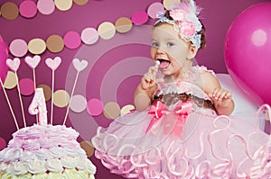 Portrait of a little cheerful birthday girl with the first cake. Eating the first cake. Smash cake