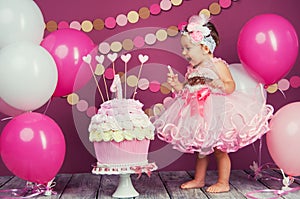 Portrait of a little cheerful birthday girl with the first cake. Eating the first cake. Smash cake