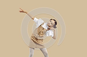 Little girl in casual beige denim pinafore dress dancing on beige studio background photo