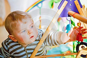 Portrait of little child, cute adorable baby boy playing with colorful toys. Happy, curious kid at home, indoors.