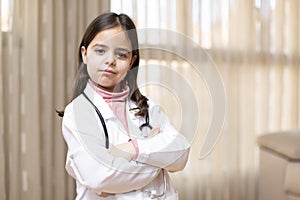 Portrait of little child in doctor`s uniform posing with crossed arms and responsible attitude. Concept of medicine and health