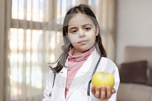 Portrait of little child dressed as a nurse showing an apple in her hand. Concept of wellbeing and healthy life