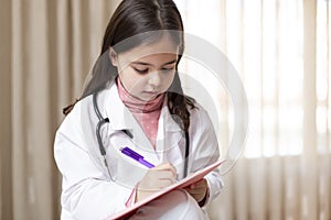 Portrait of little child dressed as a nurse writing concentrated in a notebook