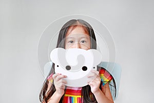 Portrait of little child girl holding blank white animal paper mask fronting her face on white background. Idea and concept for