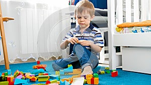 Portrait of little concentrated boy palying on carpet with toy blocks