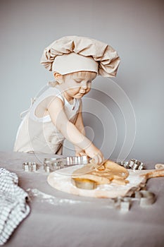 Portrait of a little cook kneading dough in an apron and a chef& x27;s hat.