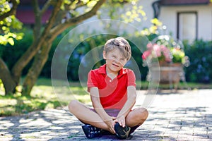 Portrait of little cool kid boy sitting on ground on sunny day in domestic backyard. Happy healthy child having fun on