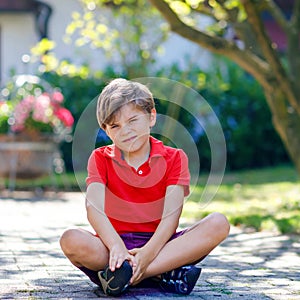 Portrait of little cool kid boy sitting on ground on sunny day in domestic backyard. Happy healthy child having fun on