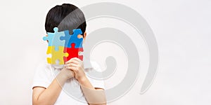 Portrait of little cute Asian child cover his face with the colorful jigsaw puzzles pieces in white background