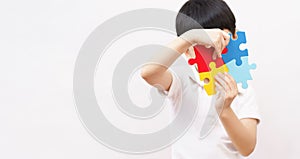 Portrait of little cute Asian child cover his face with the colorful puzzles pieces in white background