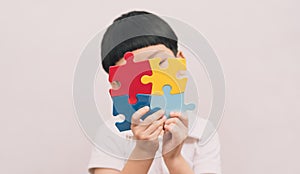 Portrait of little cute Asian child cover his face with the colorful puzzles pieces in white background