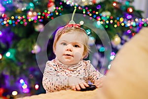 Portrait of little cute baby girl learning walking and standing. with Chrismas tree and lights on background. Adorable