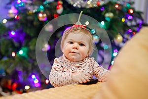 Portrait of little cute baby girl learning walking and standing. with Chrismas tree and lights on background. Adorable