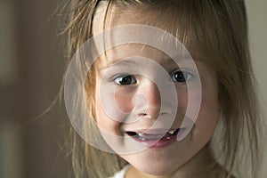 Portrait of little cute blond young child girl with gray eyes smiling in camera with funny toothless smile on blurred gray backgro