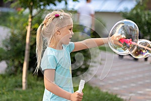 Portrait of little cute caucasian blond girl having fun and joy blowing big soap bubbles playing on city street park outdoors.