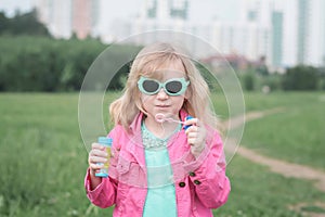 Portrait of little cute caucasian blond girl having fun and joy blowing big soap bubbles playing on city street park outdoors