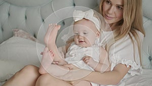 Portrait of a little cute girl. The child sits on his mother`s lap and plays. A young mother holds the plump legs of her