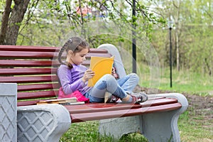 Portrait of little cute girl with open book is sitting on the wooden bench