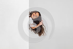 Portrait of little cute smiling Caucasian girl peeking around the corner  over white studio background.