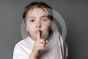 Portrait of a little cute teenage girl showing a sign of silence with a finger to her mouth. The Girl Has a Secret