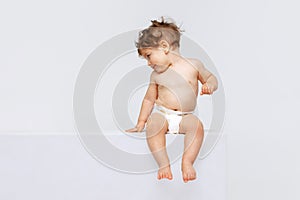 Portrait of little cute toddler boy, baby in diaper joyfully sitting and laughing isolated over white studio background