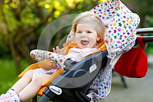 Portrait of little cute toddler girl sitting in stroller or pram and going for a walk. Happy cute baby child having fun