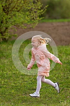 Portrait of little European girl with blonde hair in pink outfit running across field. Vertical frame