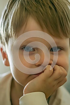 portrait of a little fair-haired boy with his chin propped on his hand and looking at the camera.