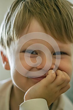 Portrait of a little fair-haired boy with his chin propped on his hand and looking at the camera.