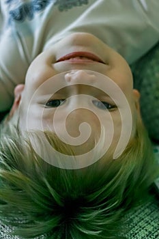 Portrait of a little fair-haired cheerful boy lying upside down.