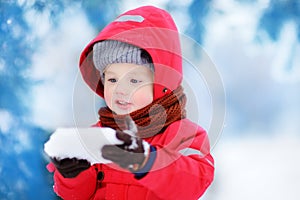 Portrait of little funny boy in red winter clothes having fun with piece of ice