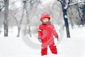 Portrait of little funny boy in red winter clothes having fun with snow during snowfall