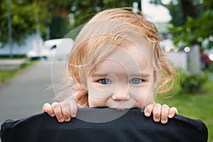 Portrait of a little funny child girl blond with blue eyes sitting in a baby stroller in the summer for greens. A funny